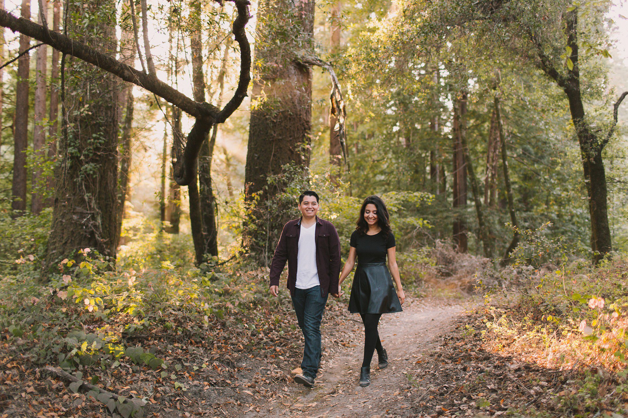 Engaged couple walking among redwood trees